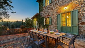 An outdoor dining area with stone walls, green shutters, and a table set for a meal.