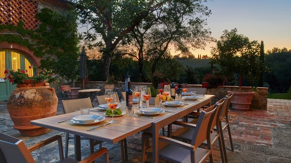 An outdoor dining area with a long table set for a meal, surrounded by chairs and potted plants.