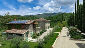 A stone house with a solar panel roof, surrounded by a well-maintained garden and a gravel path.