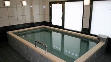 A rectangular indoor pool with a glass bottom, surrounded by dark tiles and a beige border.