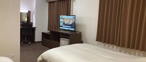 Una habitación de hotel con cama, escritorio, televisor y minibar.