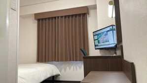 Une chambre d’hôtel avec un lit, un bureau doté d’un écran d’ordinateur et une grande fenêtre avec des rideaux.