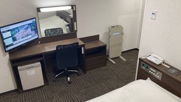 Une chambre d’hôtel équipée d’un lit, d’un bureau avec un ordinateur, d’une chaise, d’un petit réfrigérateur et d’un téléphone.