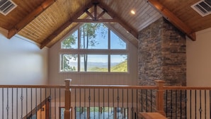 A spacious room with a high ceiling, wooden beams, and a large window offering a view of the outdoors. - Mountain Creek View-Hot Tub - Views - Gas Firepit (Whittier)