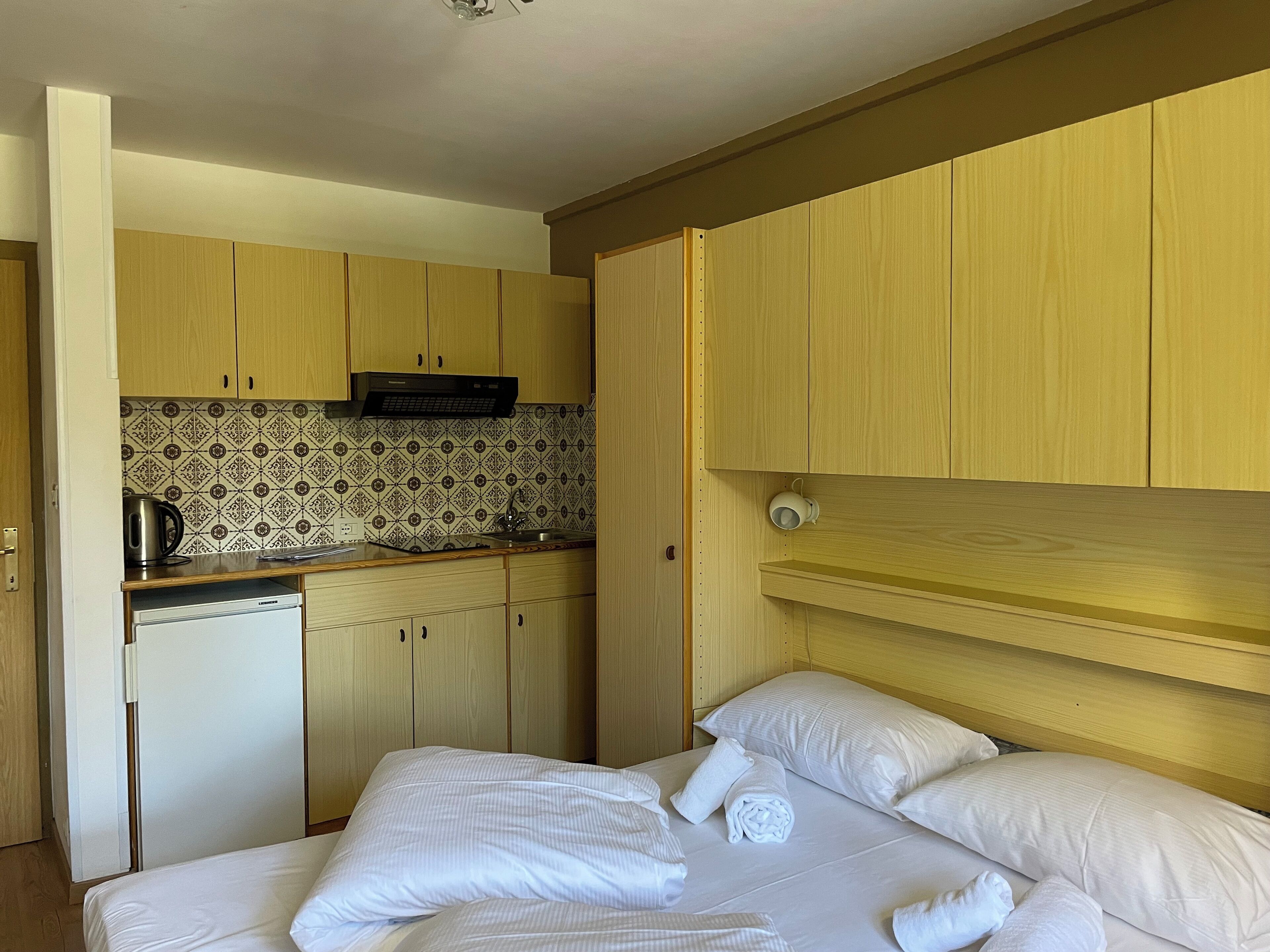 Een compacte hotelkamer met kitchenette, een bed met witte lakens en een houten hoofdbord.