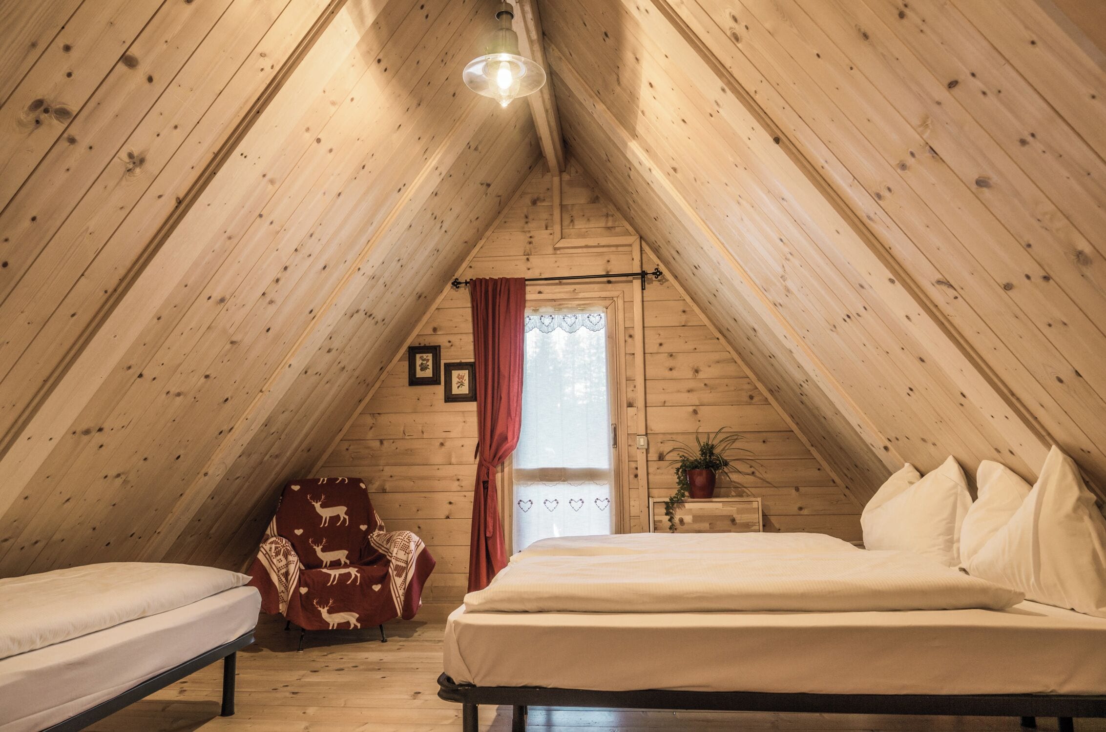 Ein gemütliches Schlafzimmer im Dachgeschoss mit schrägen Wänden, einem Bett, einem Sessel und einem kleinen Tisch mit einer Pflanze.