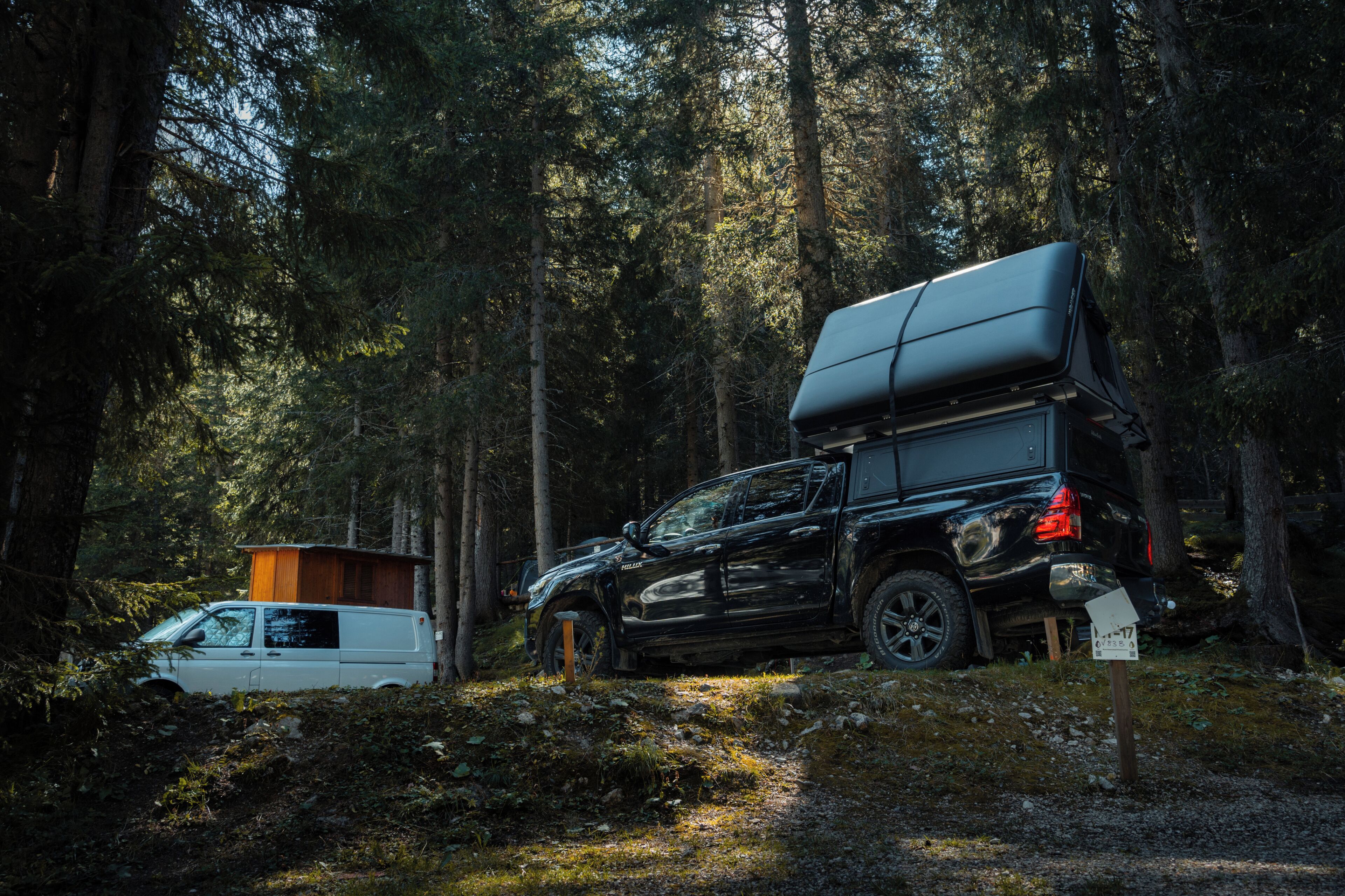 Un SUV noir avec une tente de toit est garé dans une forêt.