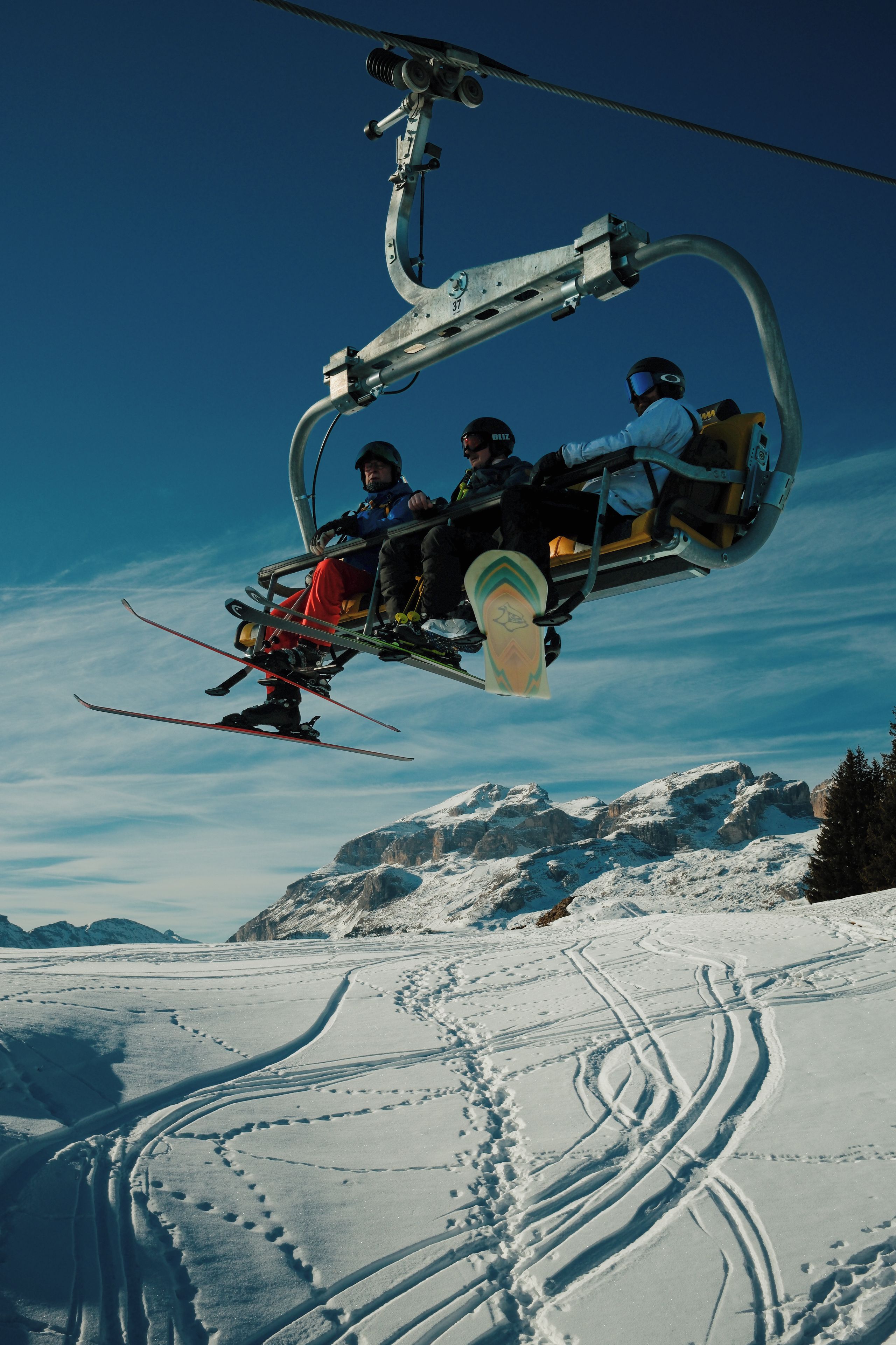 A ski lift carrying skiers with visible ski tracks on the snow below.