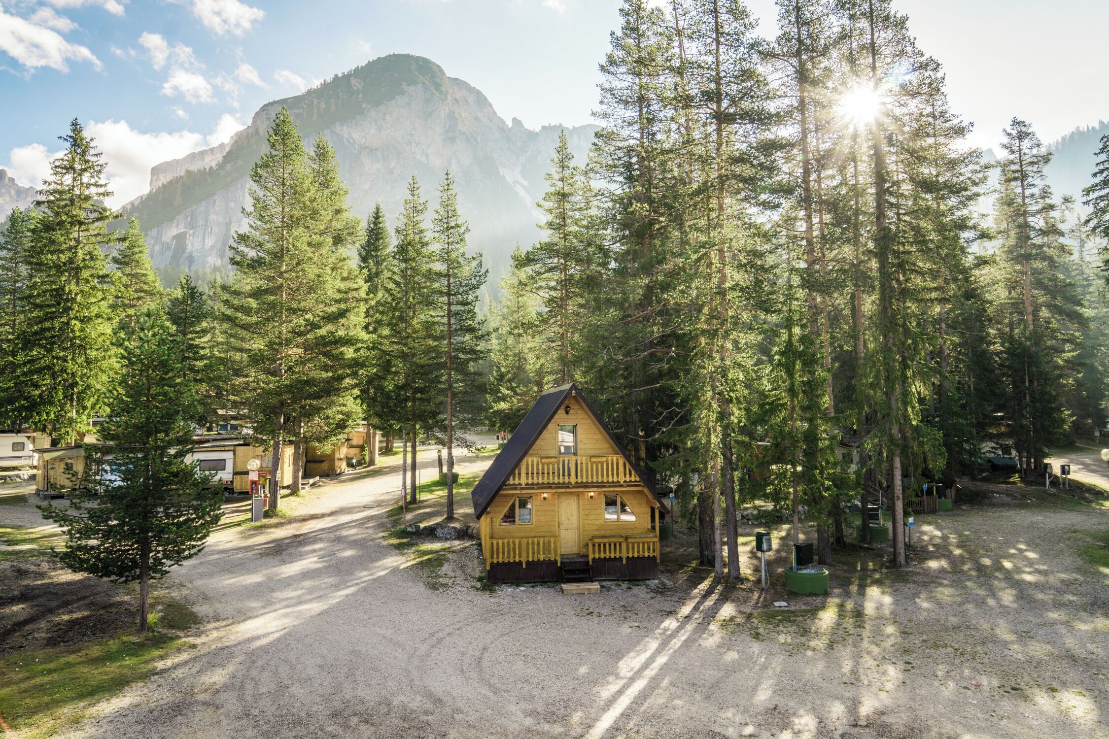 A cabin with a two-story structure, surrounded by tall pine trees and a mountain backdrop.