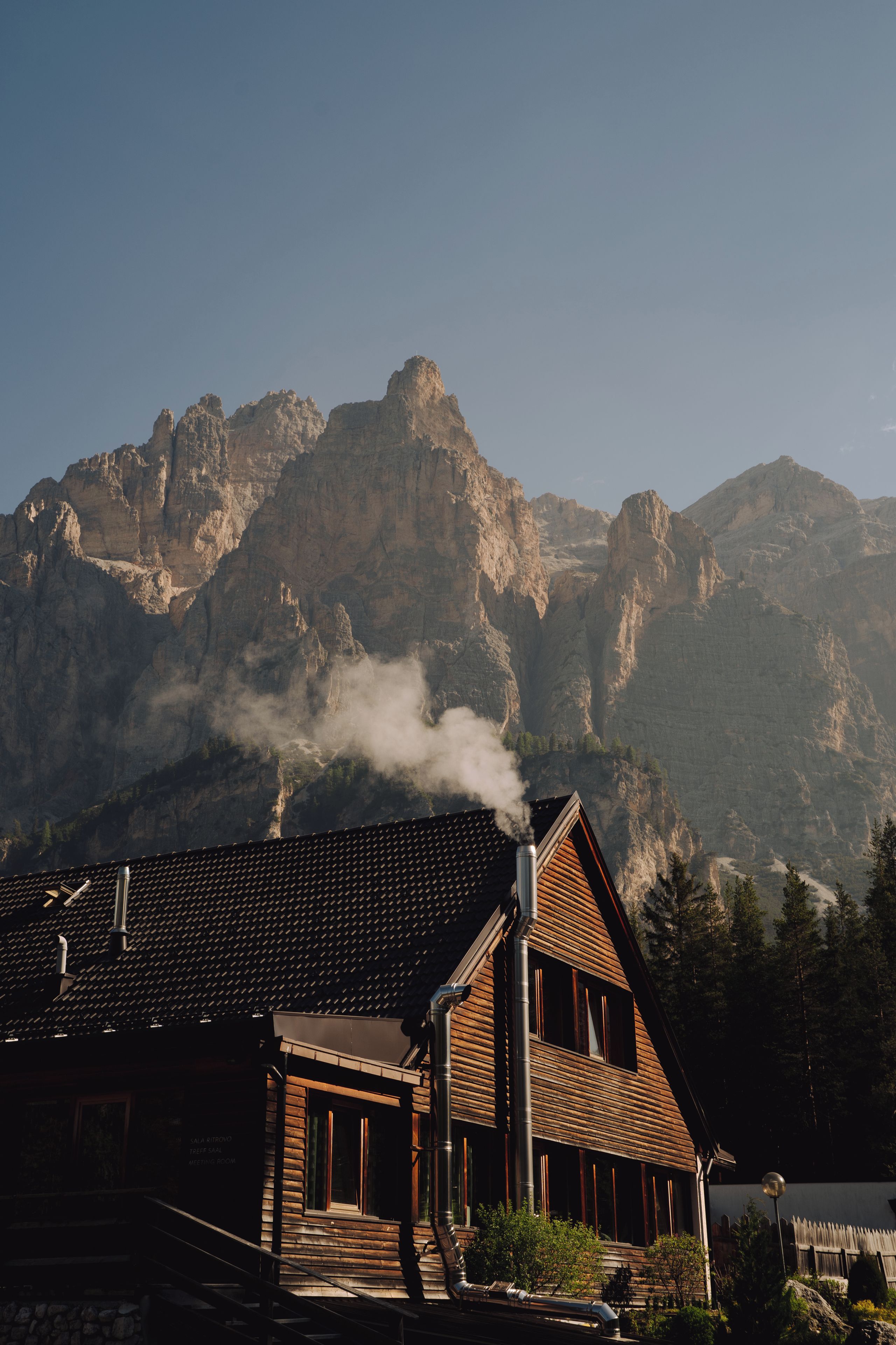 Una cabaña con chimenea que emite humo, rodeada de un paisaje montañoso.