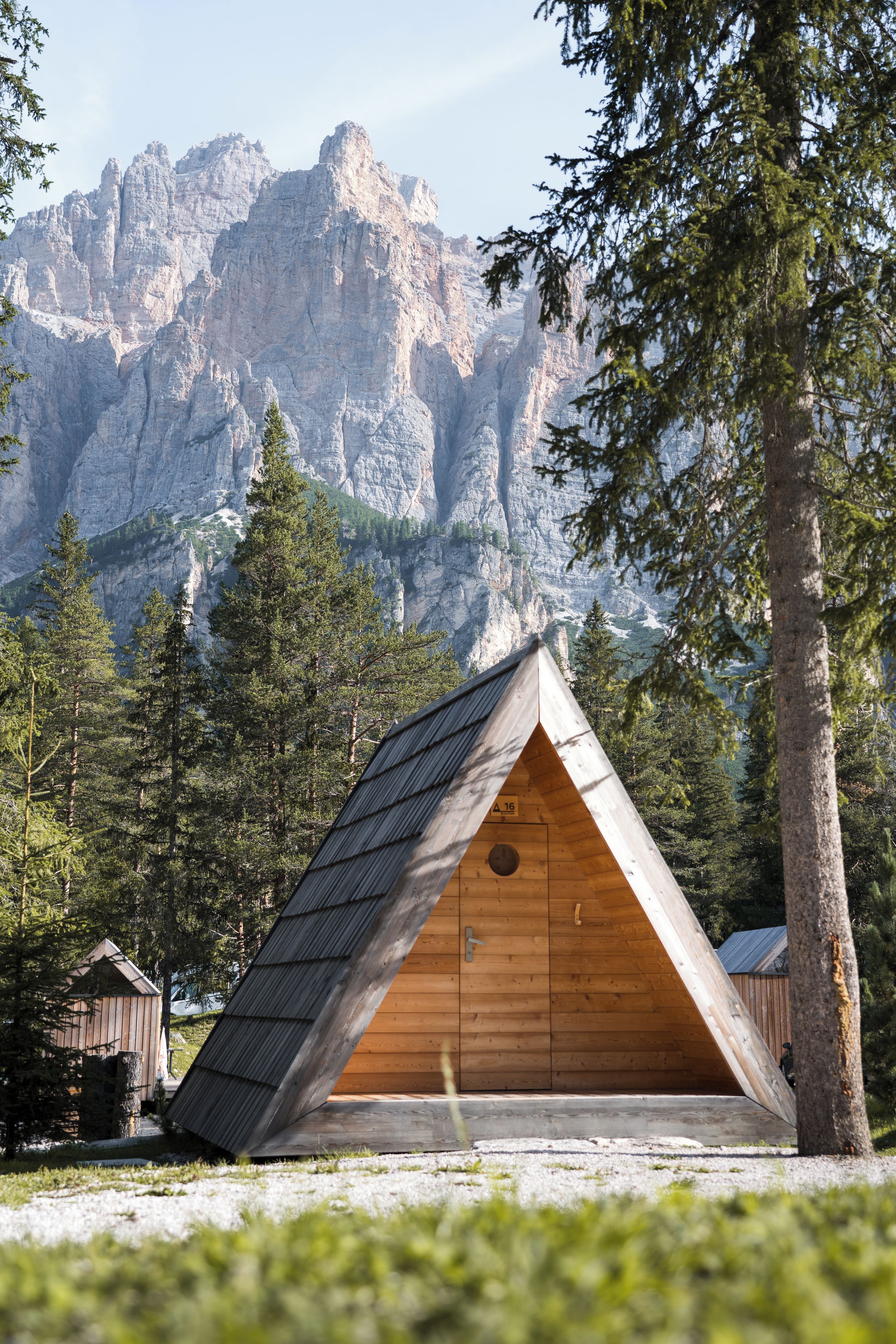 A wooden cabin with a sloped roof, surrounded by a forest and mountains in the background.