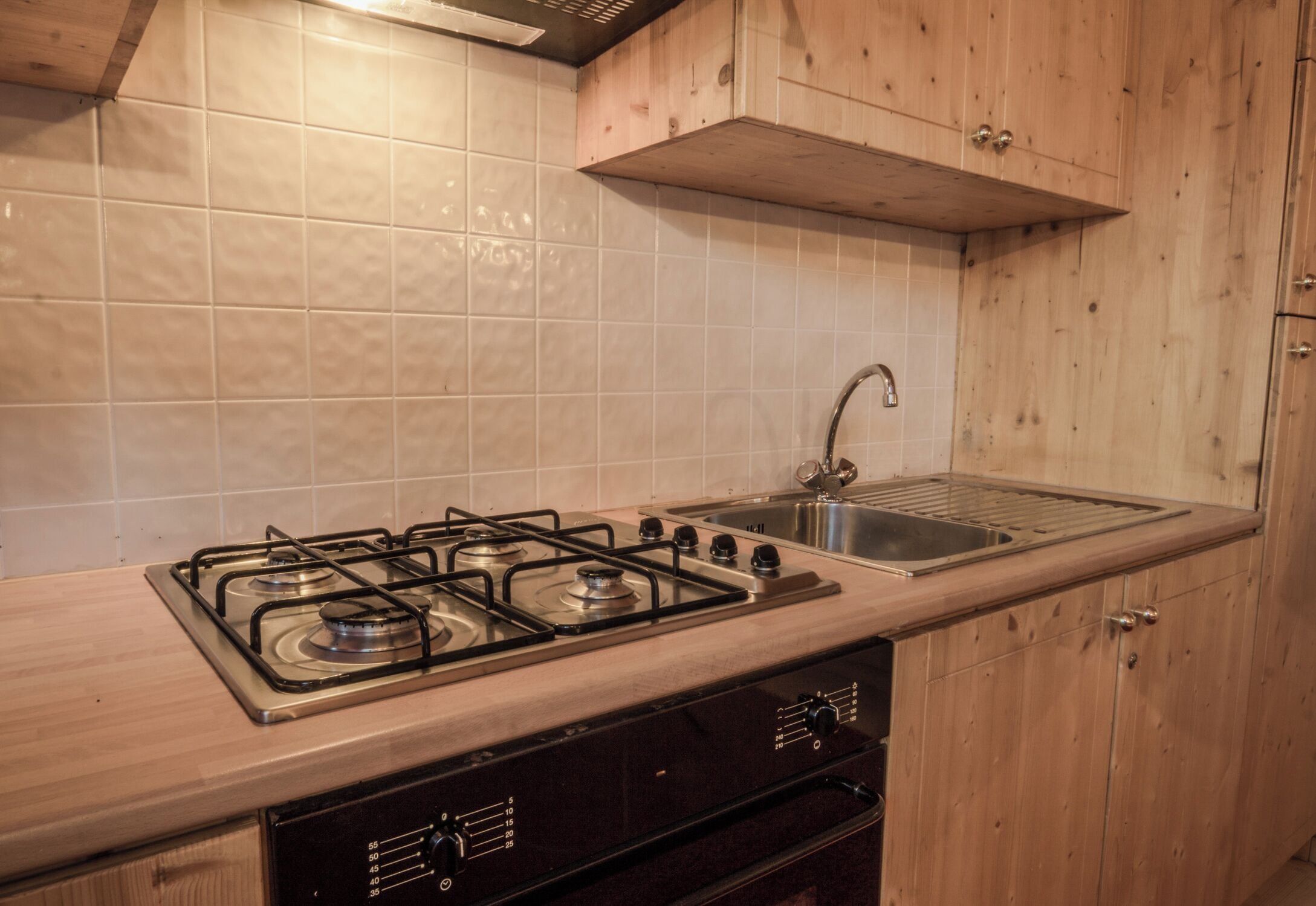 Una cocina con estufa a gas, pileta de acero inoxidable y alacenas de madera.