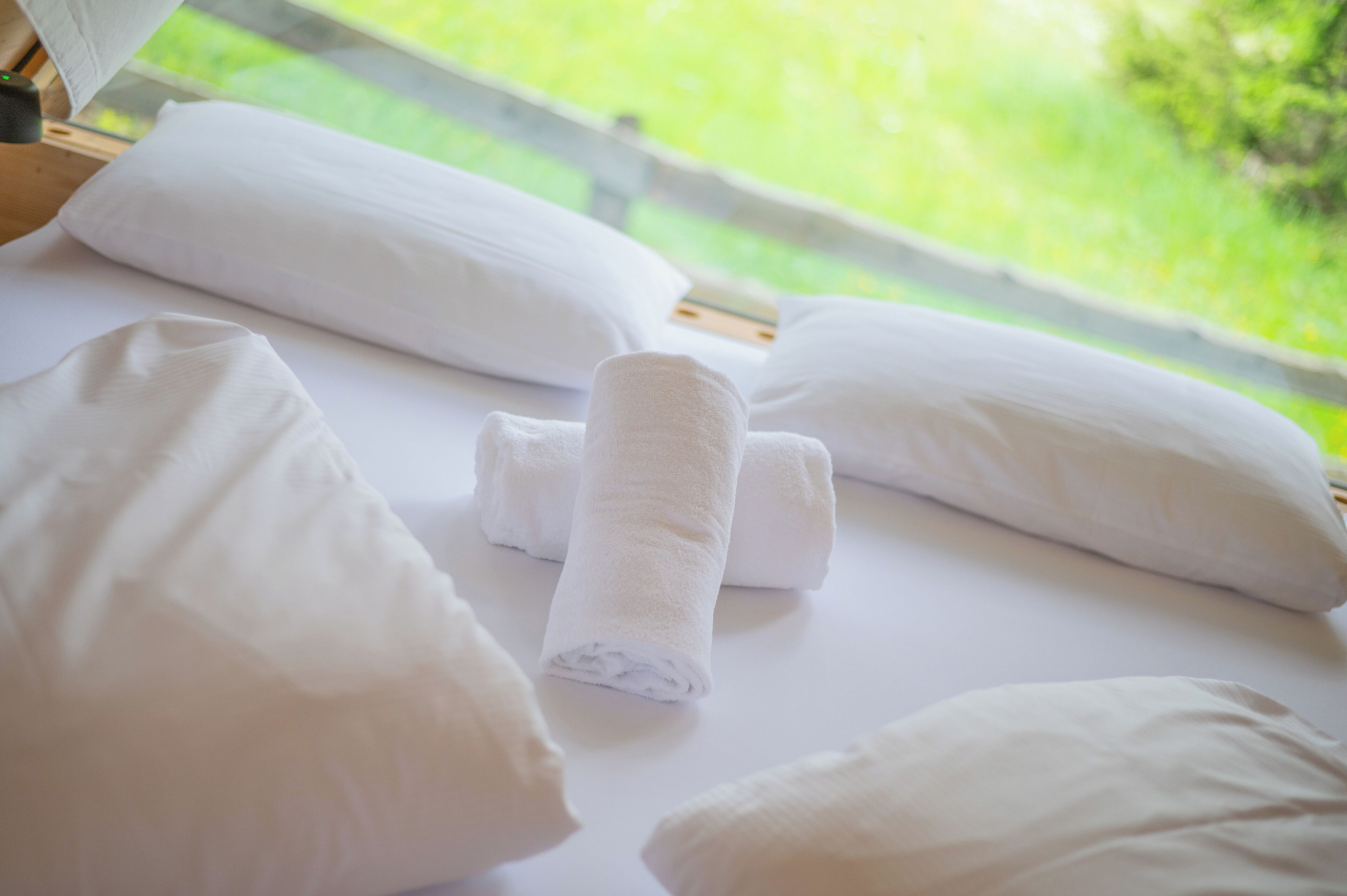A neatly made bed with white pillows and a rolled towel.