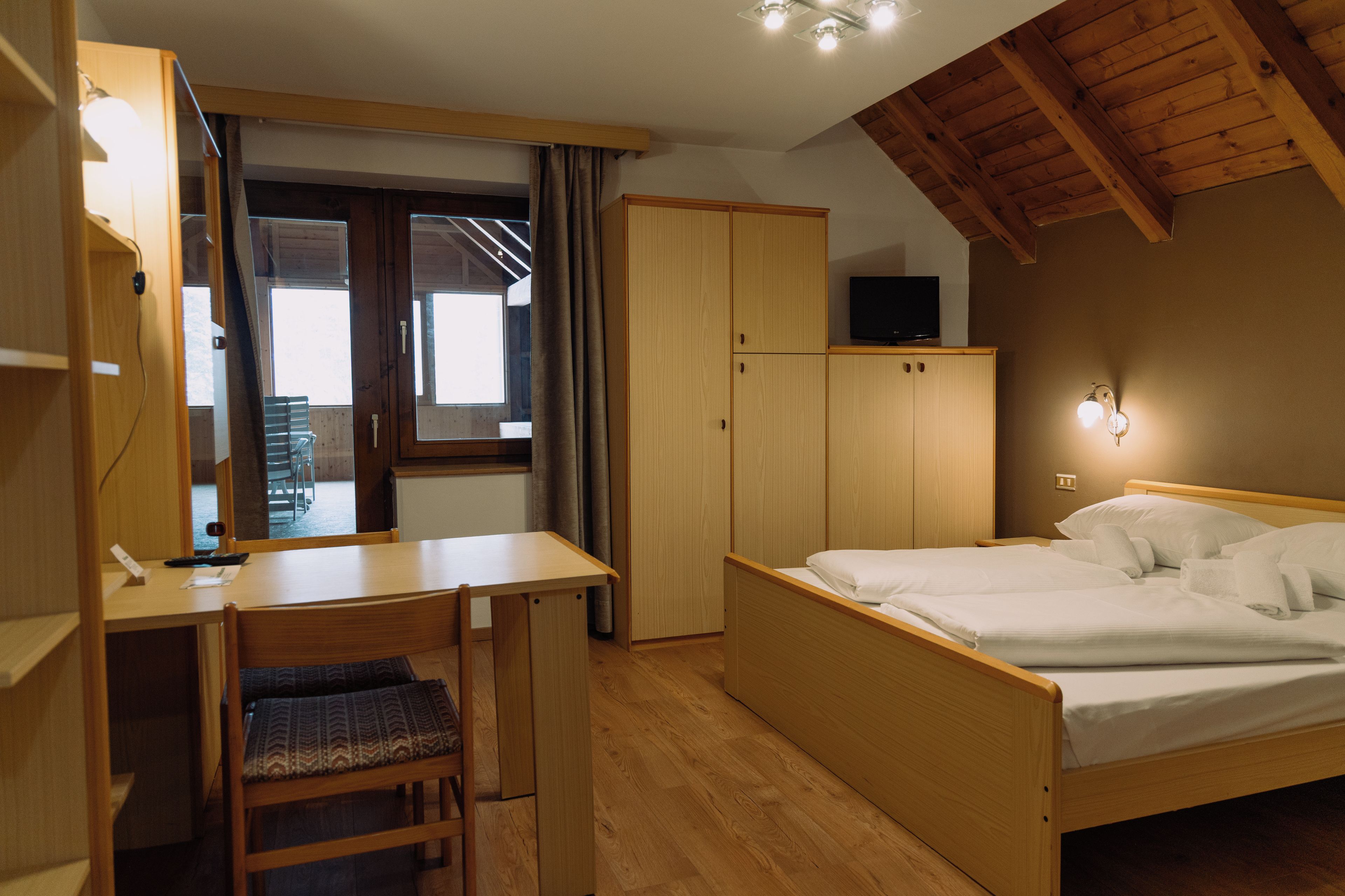 Una habitación con una cama, un escritorio y una silla. Hay un armario y un televisor en una estantería.