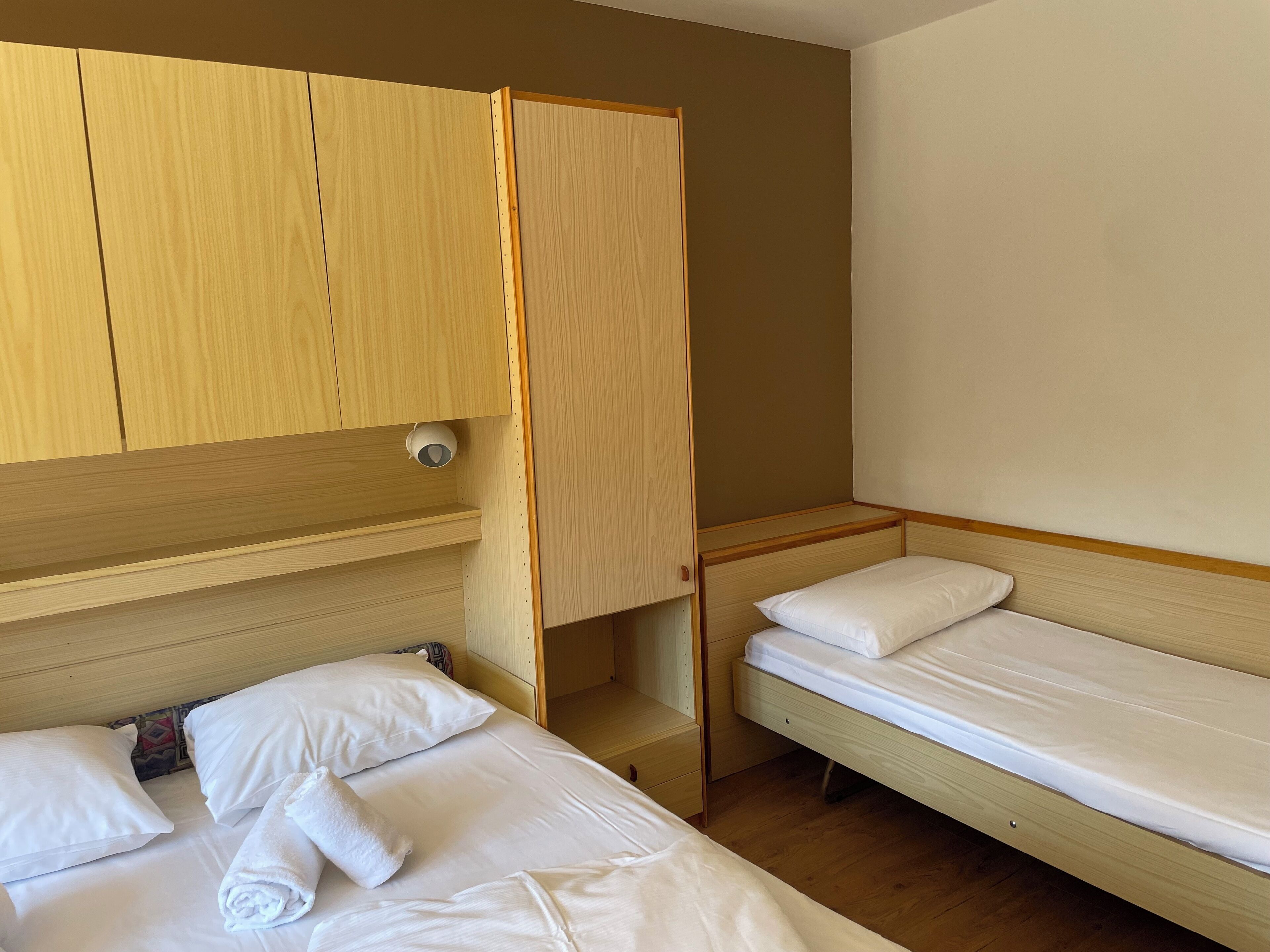 Een compacte hotelkamer met twee eenpersoonsbedden, houten kledingkasten en een klein nachtkastje.