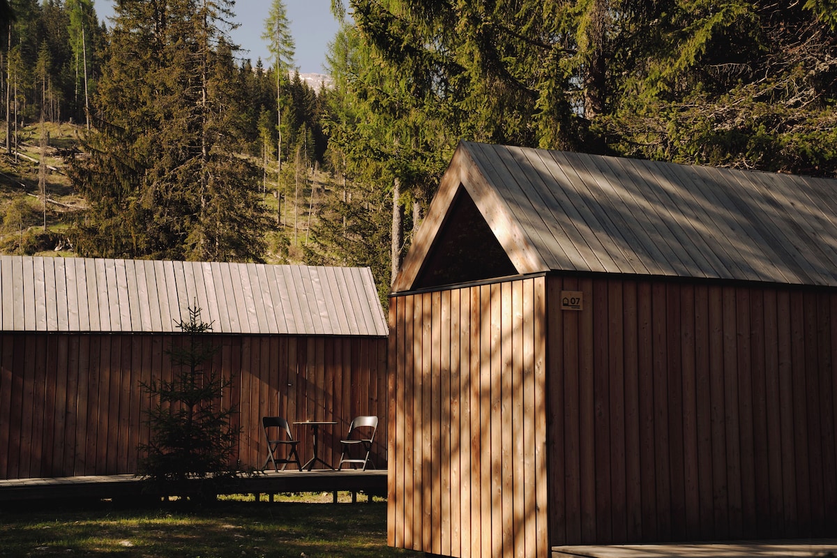 A wooden cabin with a metal roof, a small table, and two chairs outside.