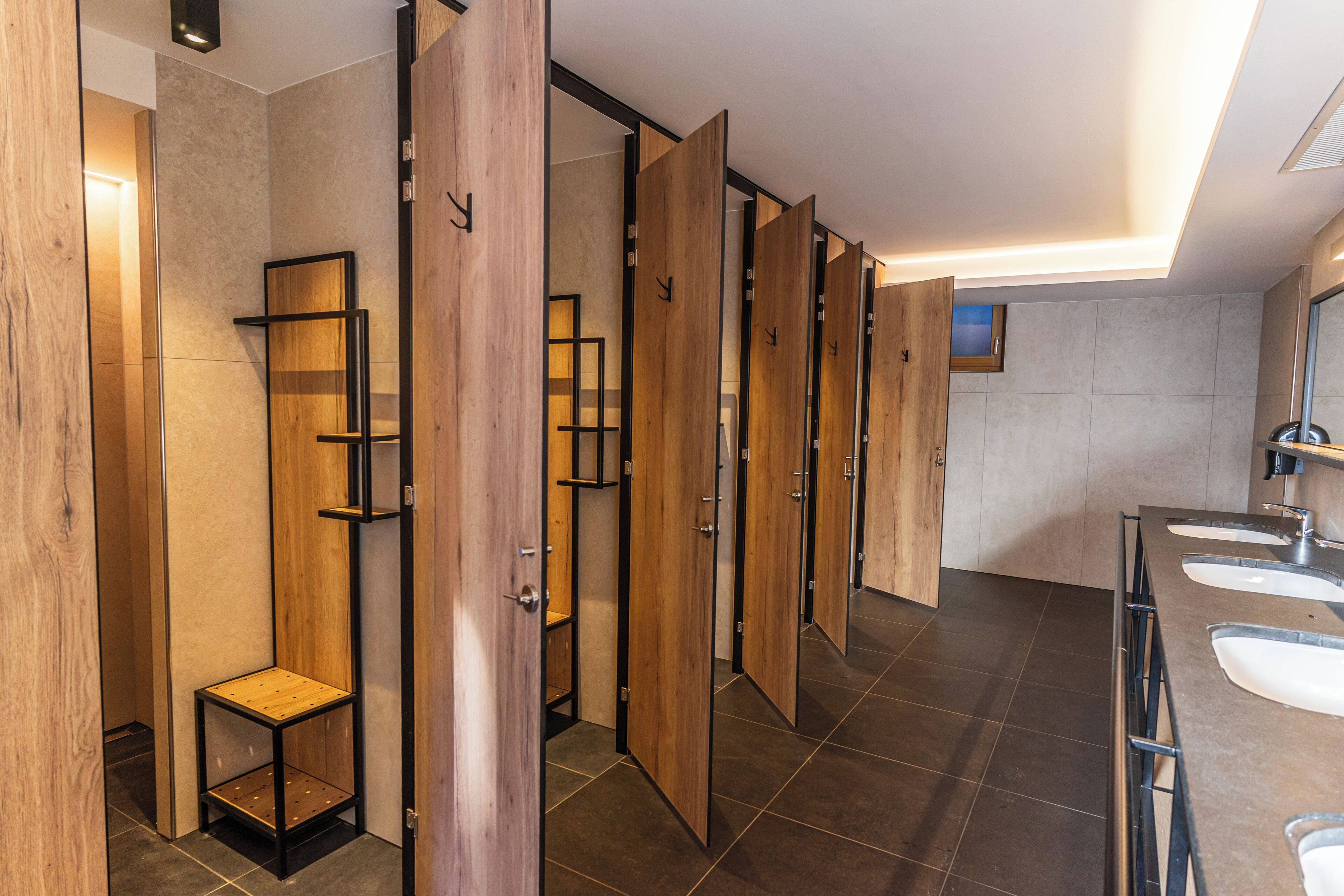 A modern bathroom with wooden partitions, a small wooden stool, and multiple sinks.