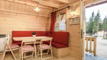L’intérieur d’un chalet en bois comprend une table à manger, un banc rembourré de coussins rouges et offre une vue sur la forêt.