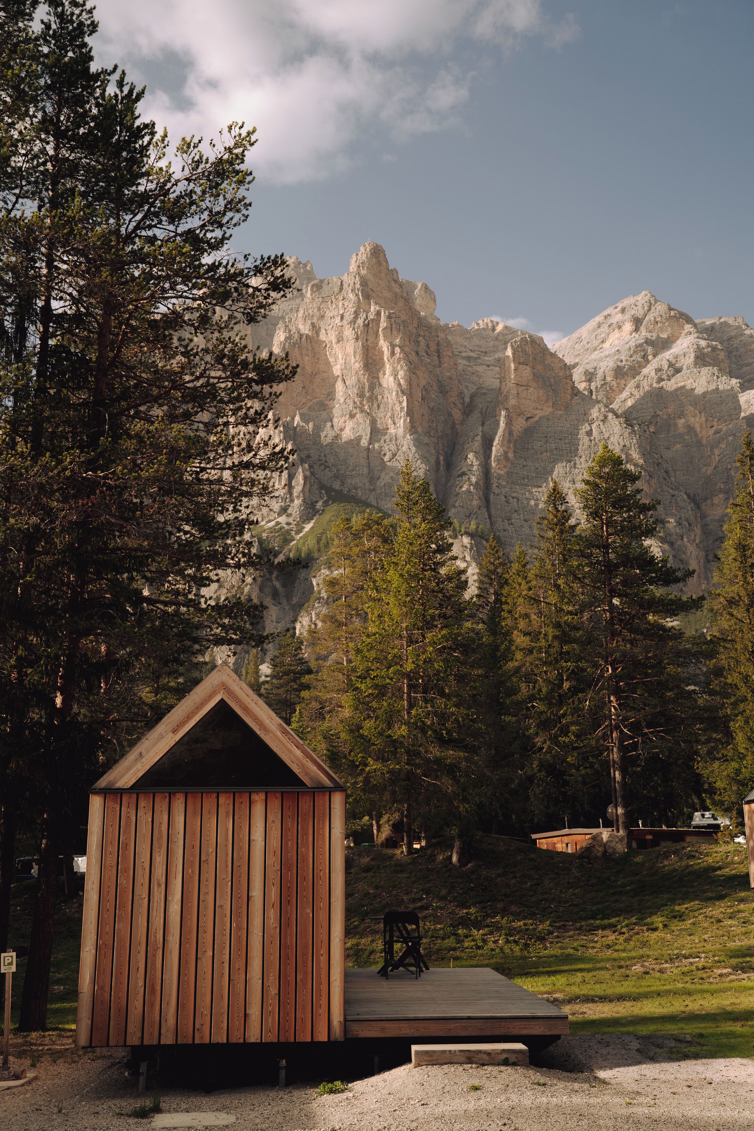 A wooden cabin with a deck, surrounded by trees and mountains.