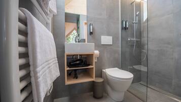 Un baño moderno con cabina de ducha de vidrio, inodoro blanco y estante de madera con toallero.