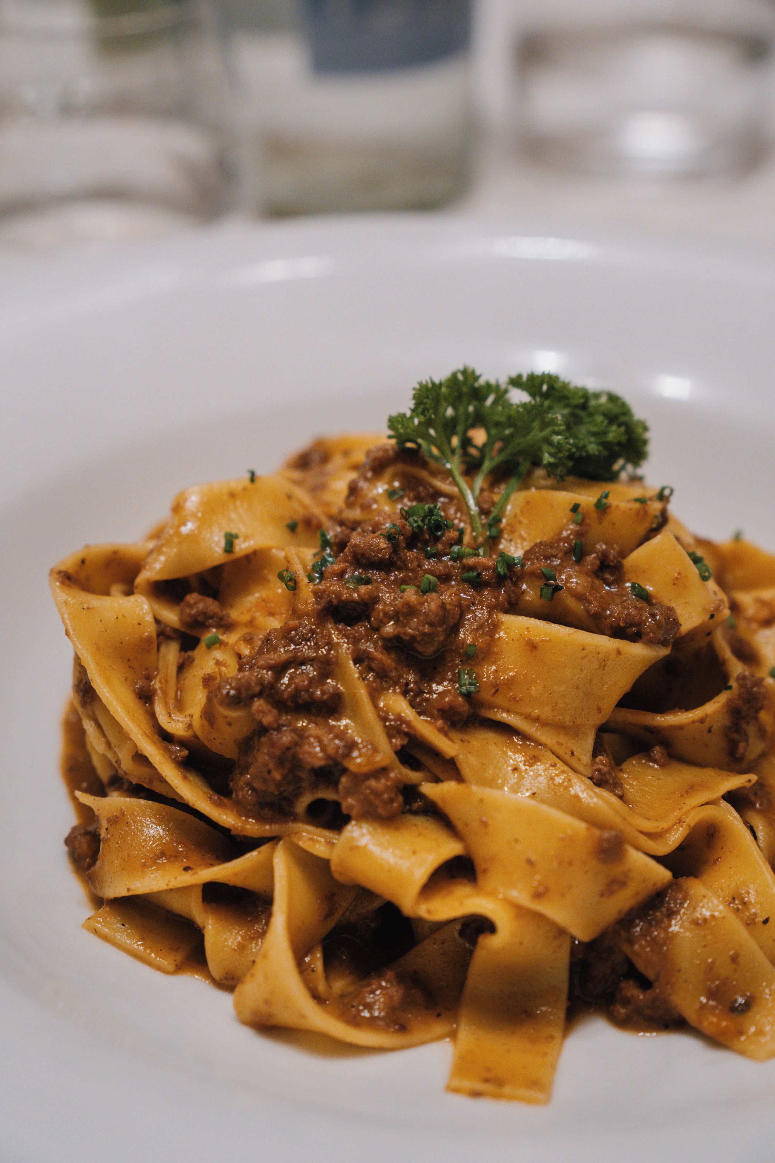 A plate of pasta with a meat sauce and a garnish of green herbs.