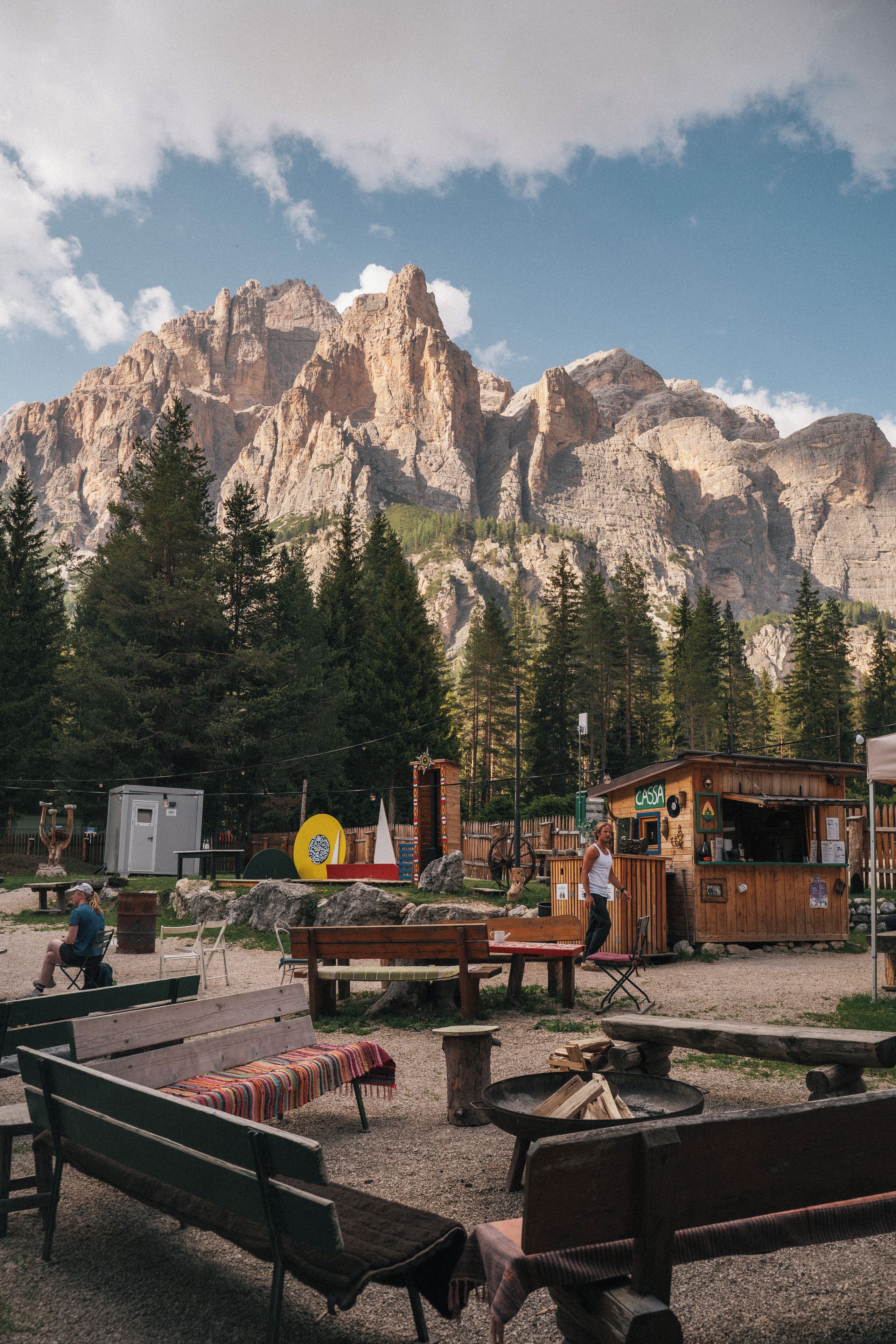 Une cabane en bois rustique, avec une pancarte indiquant « CASSA », située dans une zone montagneuse et dotée de bancs et de tables de pique-nique.