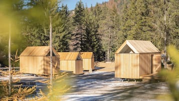 Three wooden cabins with pitched roofs, surrounded by a forested area and a body of water.