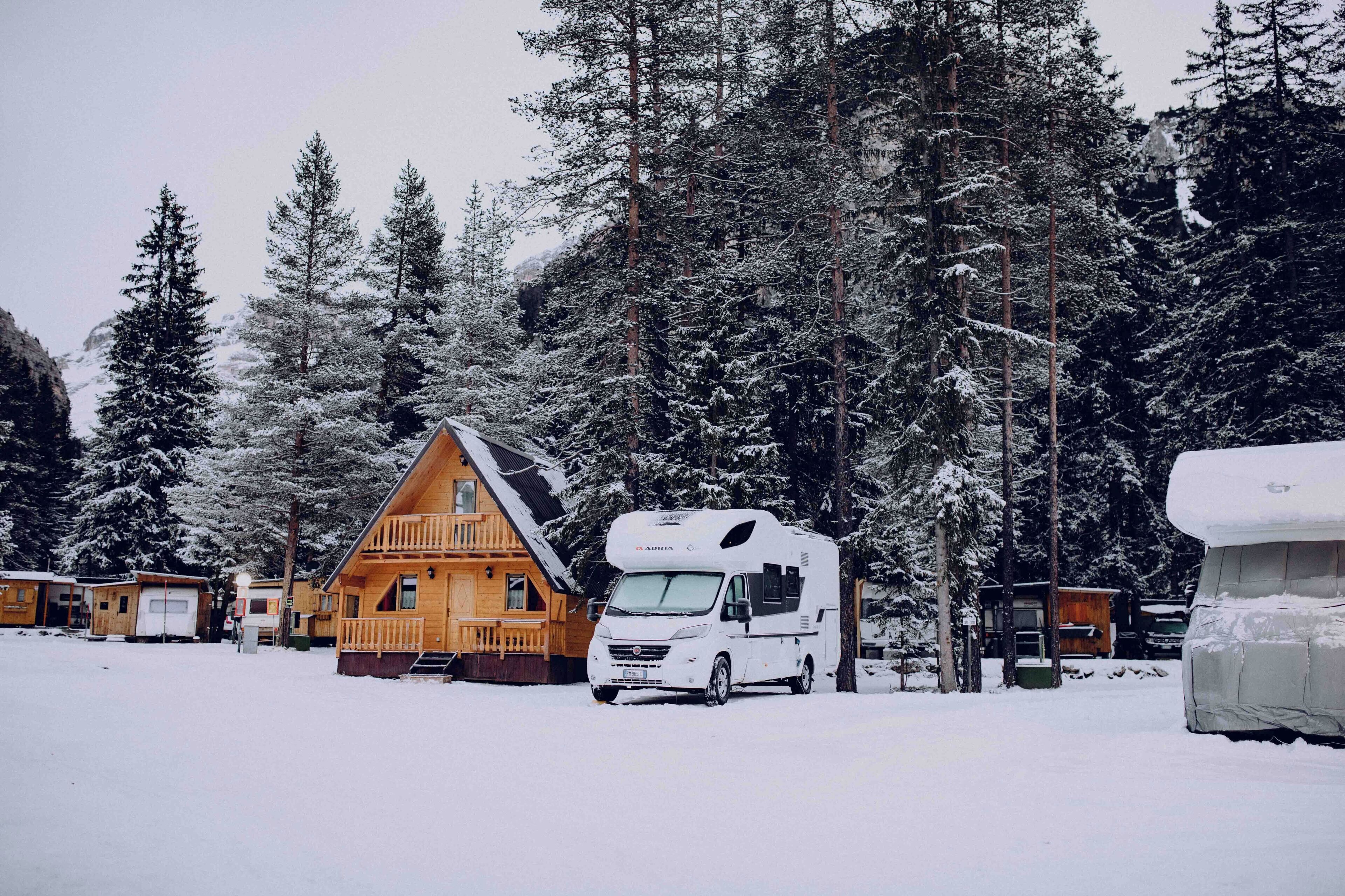 Un terrain de camping pour véhicules récréatifs, recouvert de neige, avec un grand véhicule récréatif et une cabane.