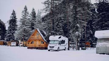 Un terrain de camping pour véhicules récréatifs, recouvert de neige, avec un grand véhicule récréatif et une cabane.