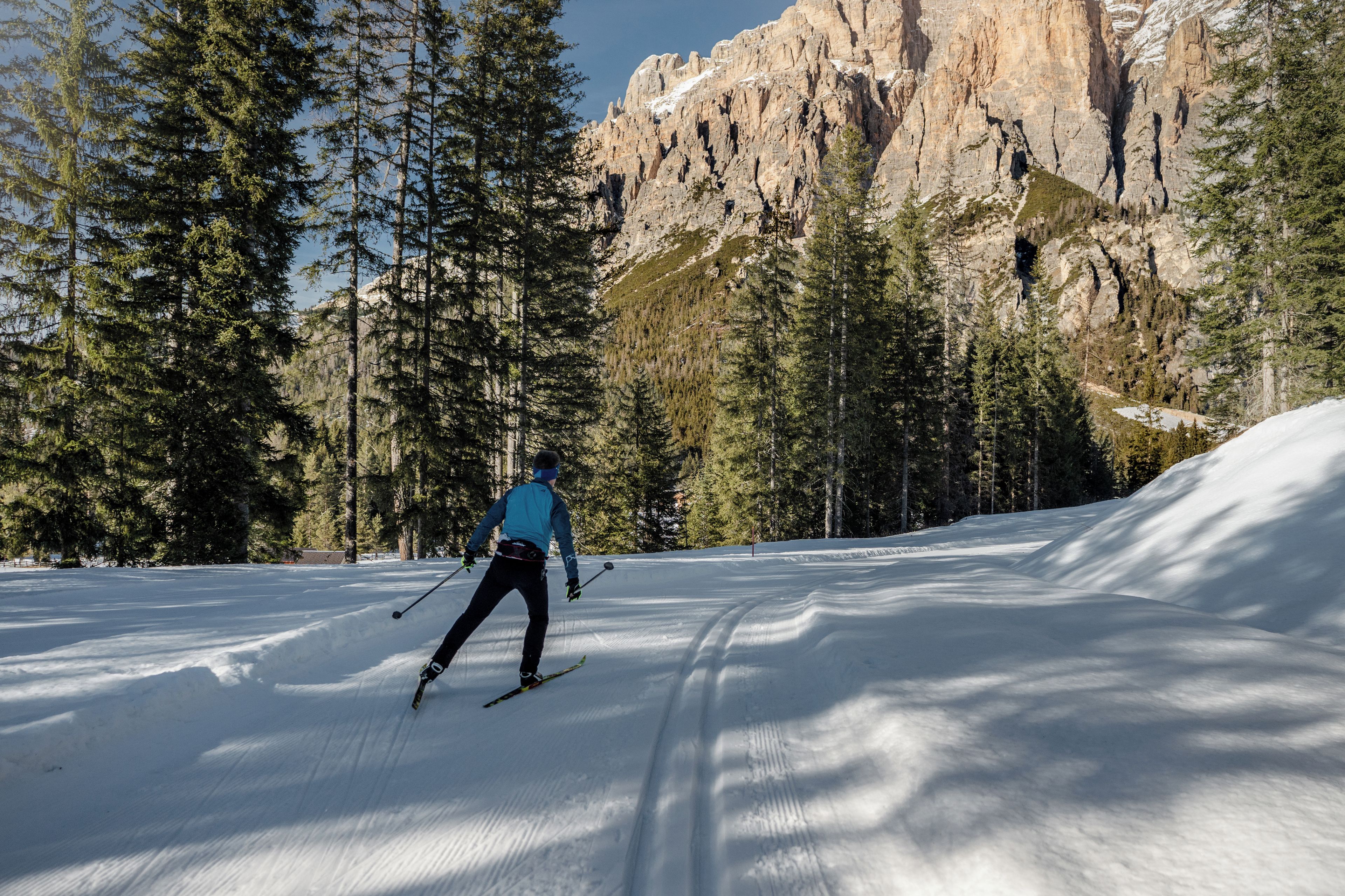 A person skiing on a snow-covered slope with a mountainous backdrop and dense forest.