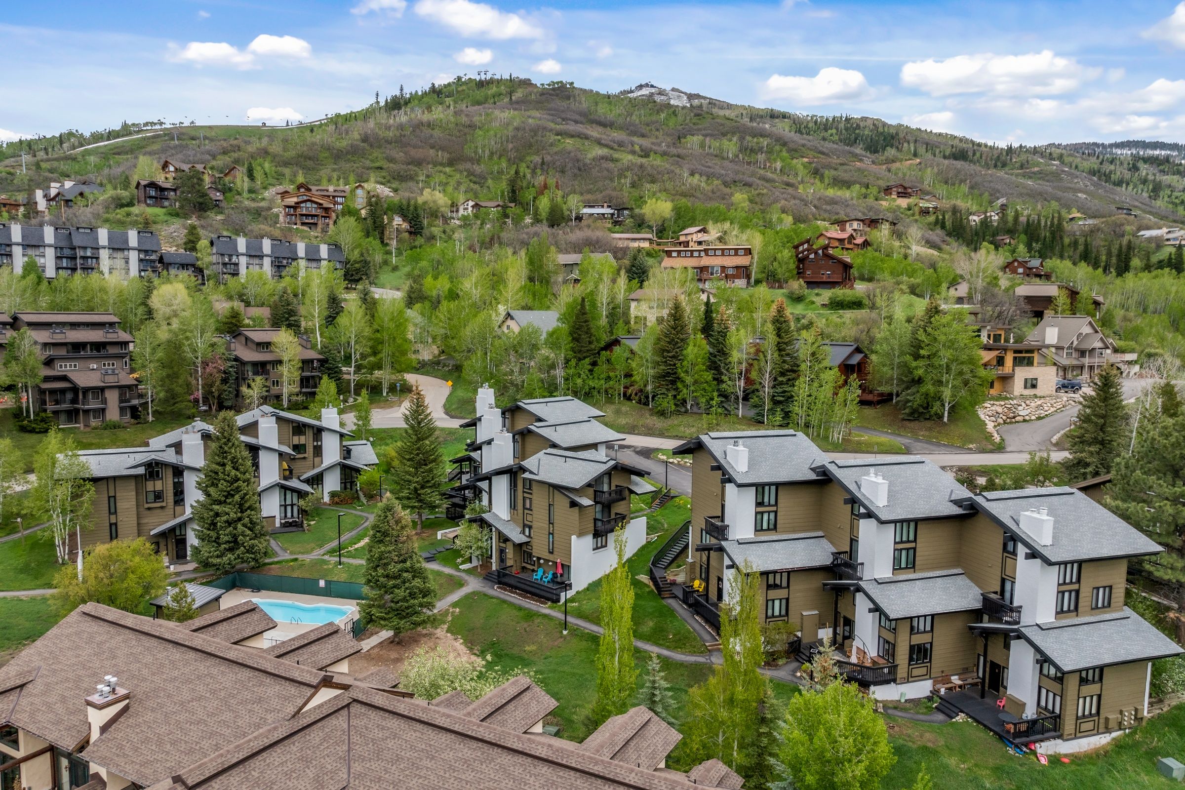 A residential area with modern houses, a swimming pool, and a hilly backdrop.