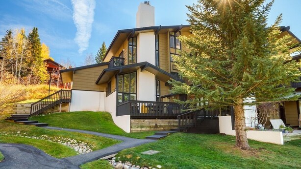 A modern two-story house with a stone pathway leading to the entrance, surrounded by a well-maintained lawn and trees. - Hillsider 7 2 Bedroom Townhouse (Steamboat Springs)