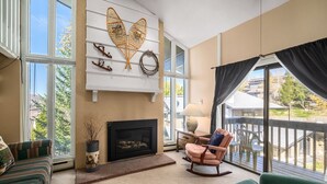 A living room with a fireplace, a rocking chair, and a view of the outdoors. - Hillsider 7 2 Bedroom Townhouse (Steamboat Springs)