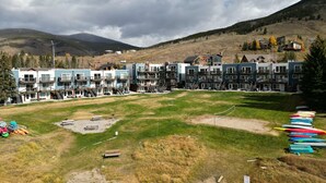 A row of modern multi-story buildings with balconies, a grassy area in front, and kayaks lined up on the right. - Yacht Club 27 1 Bedroom Condo (Dillon)