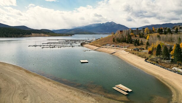A lakeside view with a marina, sandy beach, and mountains in the background. - Yacht Club 27 1 Bedroom Condo (Dillon)