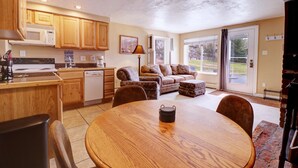 A spacious kitchen with wooden cabinets, a dining area with a round table, and a living room with a sofa and a fireplace. - Yacht Club 27 1 Bedroom Condo (Dillon)