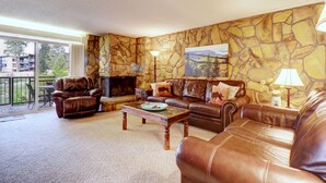 A living room with leather sofas, a fireplace, stone wall decor, and a view of the outdoors. - A105 Lake Cliffe 2 Bedroom Condo (Dillon)