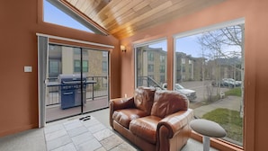 A room with a brown leather sofa, a small table, and a large sliding glass door leading to an outdoor patio with a barbecue grill. - A105 Lake Cliffe 2 Bedroom Condo (Dillon)