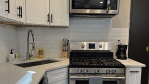 Una cocina moderna con armarios blancos, una estufa de acero inoxidable, un microondas y una cafetera.