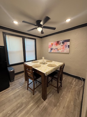 Un espace repas comprenant une table, des chaises, un ventilateur de plafond et une fenêtre avec des stores.