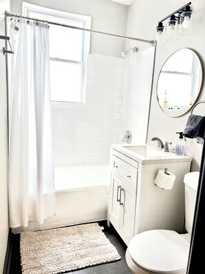 A bathroom with a shower, toilet, sink, and a mirror with a towel hanging on it.
