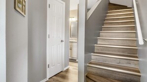 A staircase with wooden steps and a white handrail, leading to a room with a white door and a framed picture on the wall.