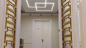 Un couloir avec une porte blanche, des panneaux muraux à motifs et un luminaire au plafond de forme géométrique.