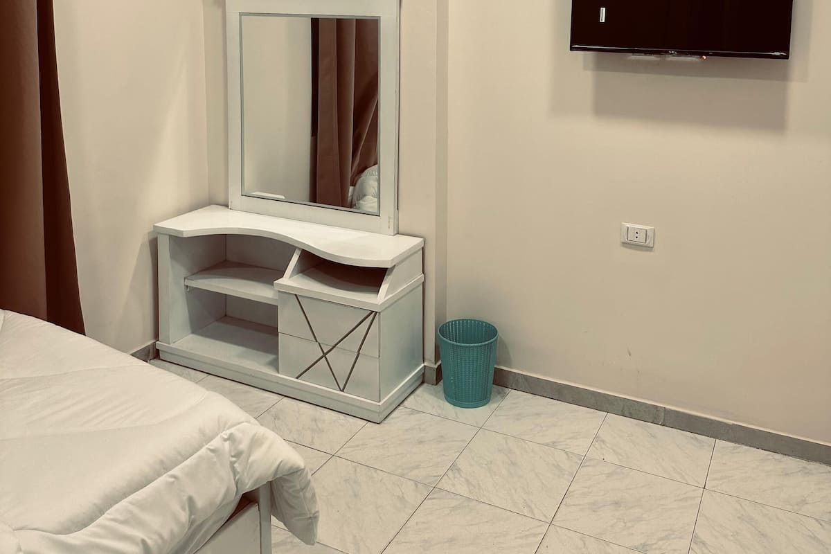 Una camera d'albergo con un letto, una toeletta con specchio, una televisione a muro e un cestino.