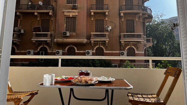 Un balcon avec une table dressée pour un repas, donnant sur un immeuble doté de nombreux balcons et présentant des détails architecturaux intéressants.