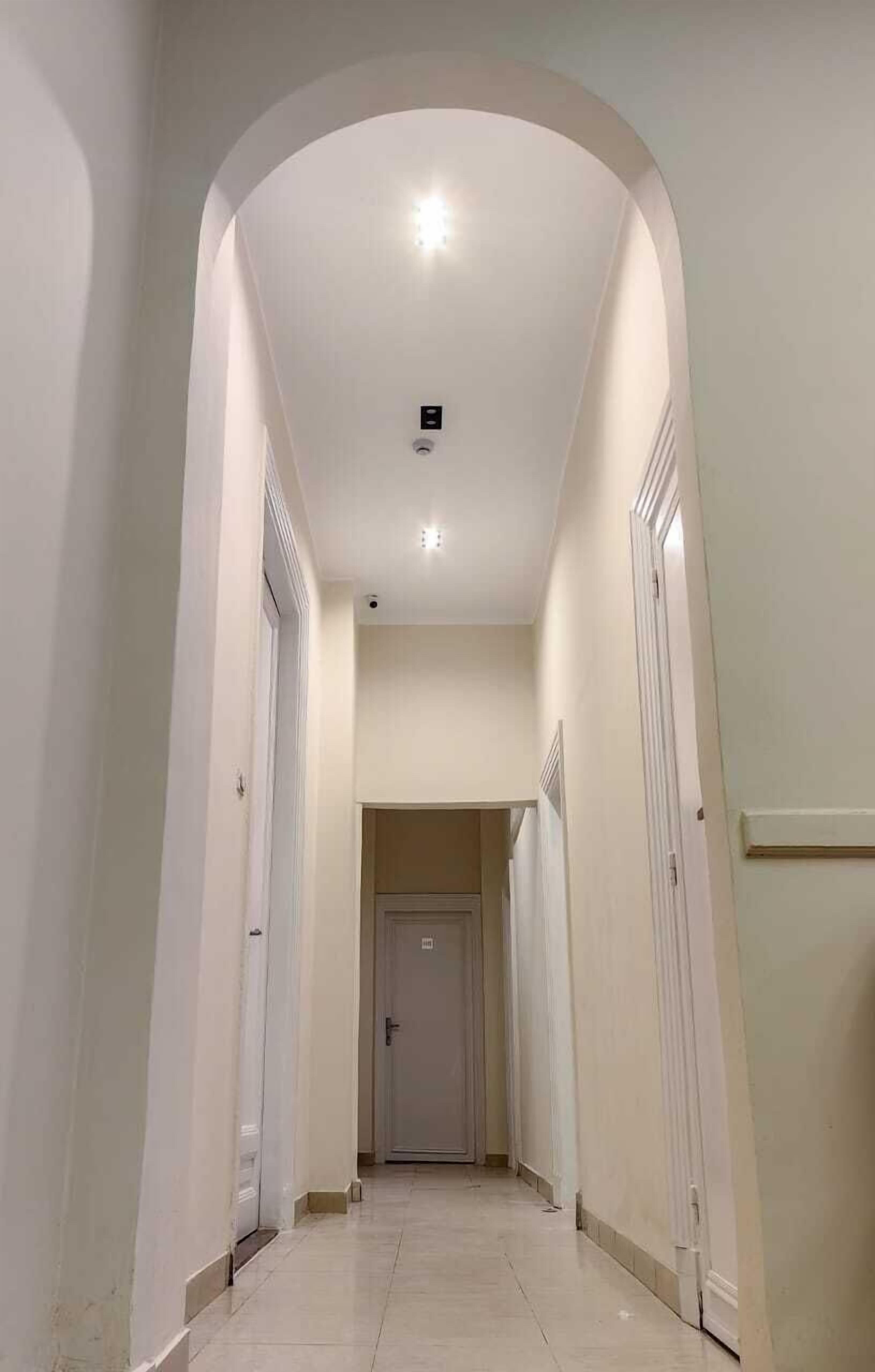 A narrow hallway with a high ceiling, white walls, and a tiled floor.