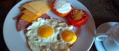 A plate with a fried egg, cheese, ham, and a tomato with a creamy topping.