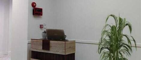 A reception area with a wooden reception desk, a potted plant, and a fire alarm on the wall.
