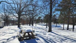 Ett snötäckt picknickbord med en bänk, omgivet av träd och en klar himmel.