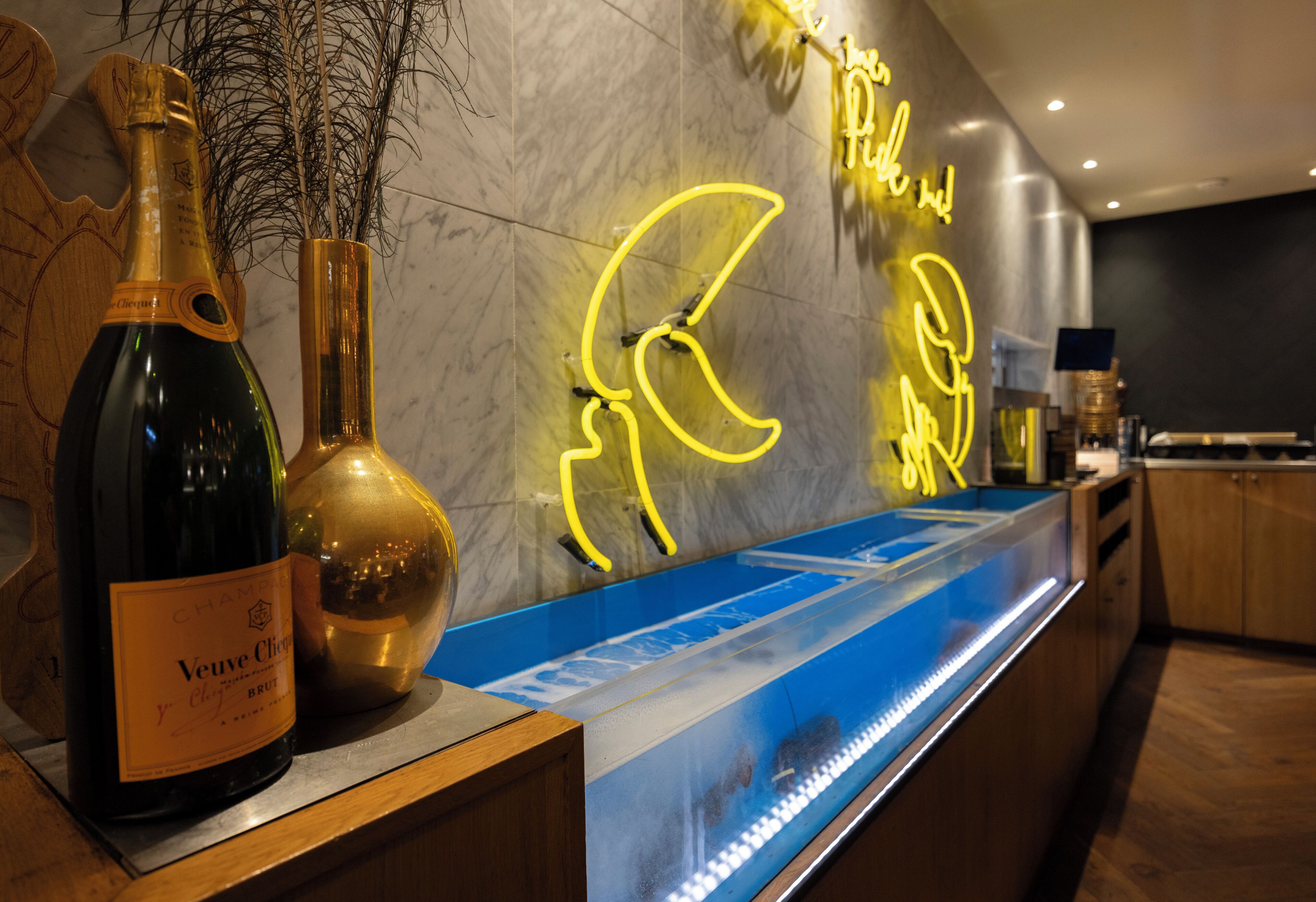 A bar area with a bottle of Veuve Clicquot champagne, a gold vase, and a neon light sign.